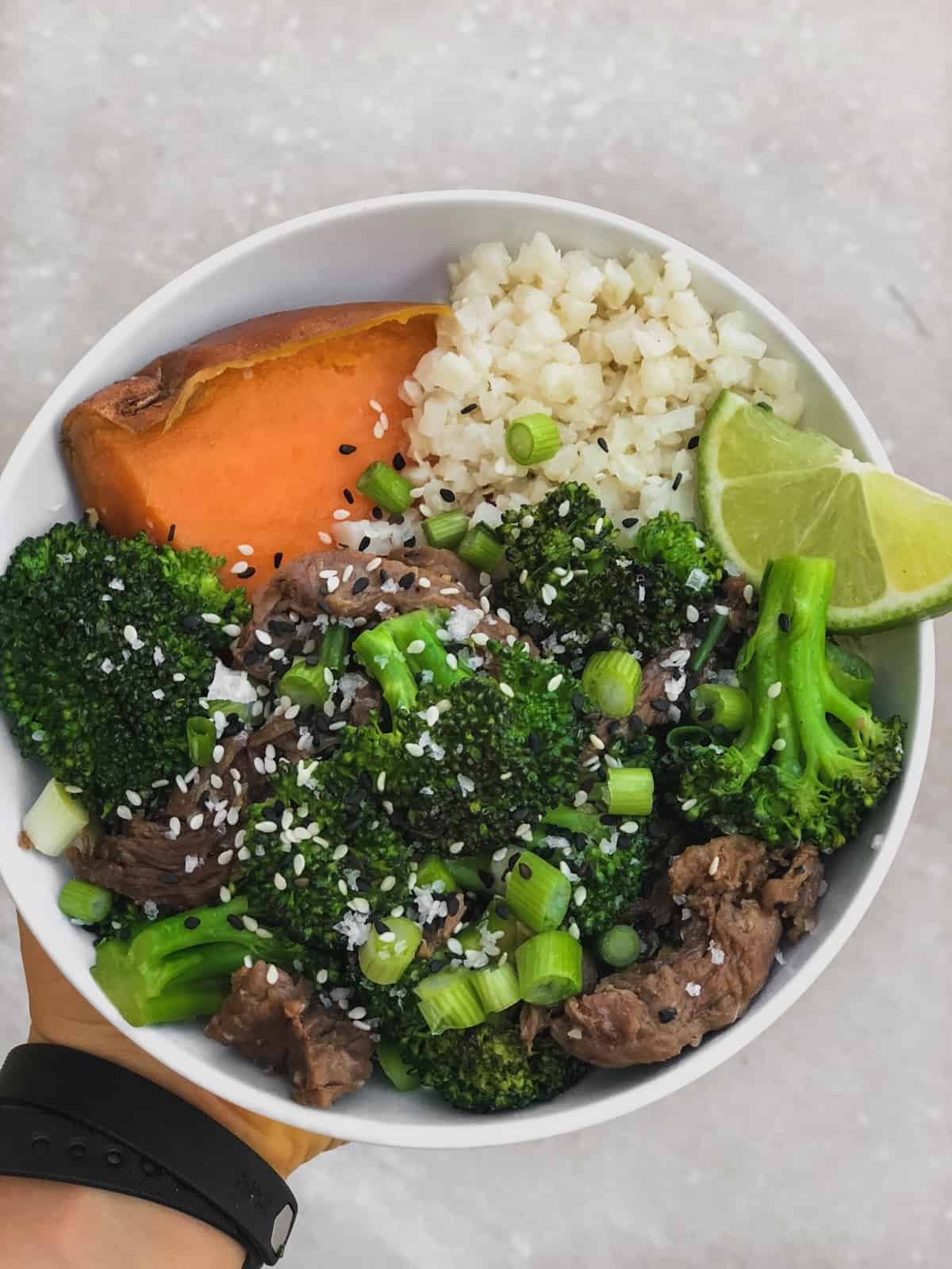 White bowl filled with half a sweet potato, cauliflower rice, and beef and broccoli