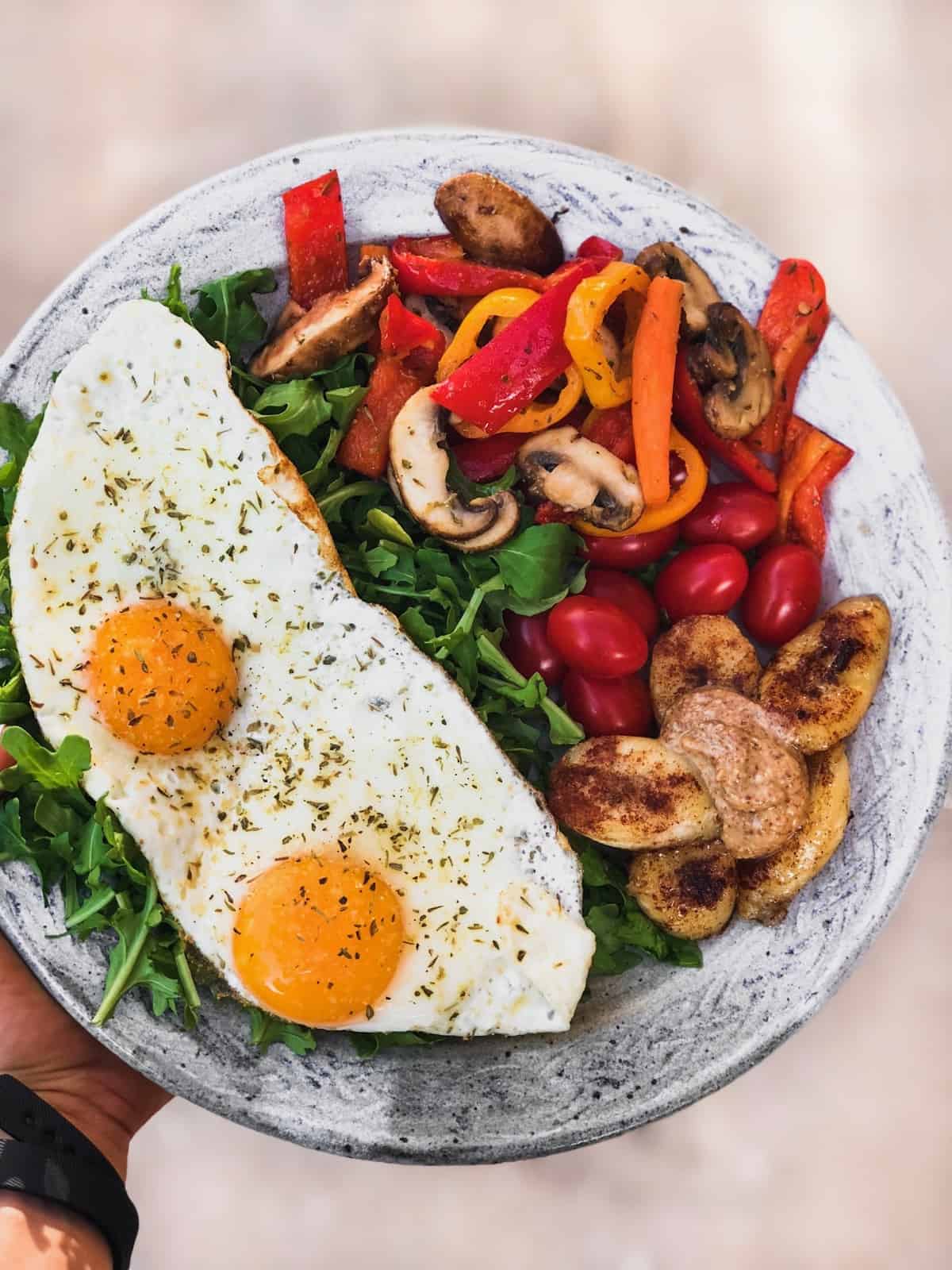 Plate of greens, 2 fried eggs, sautéed veggies, and a sautéed banana with almond butter