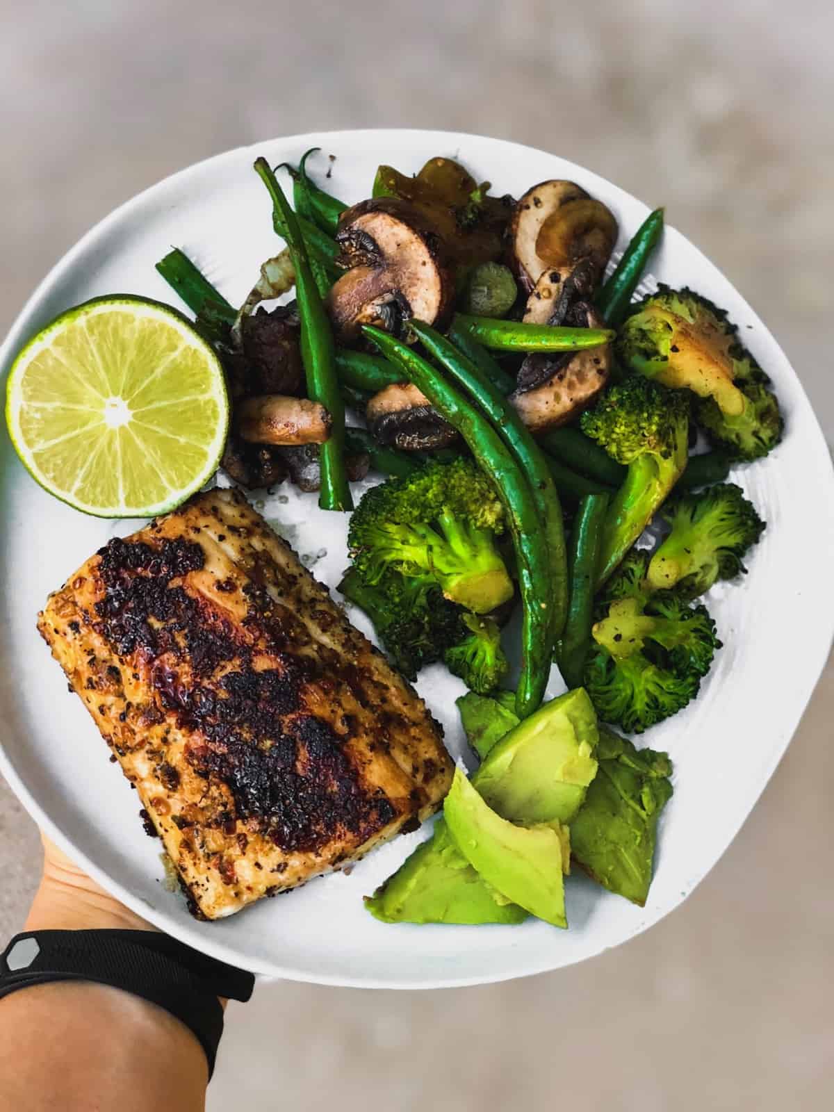 Plate of sautéed green beans, broccoli, and mushrooms, avacado, and blackened fish with half a lime