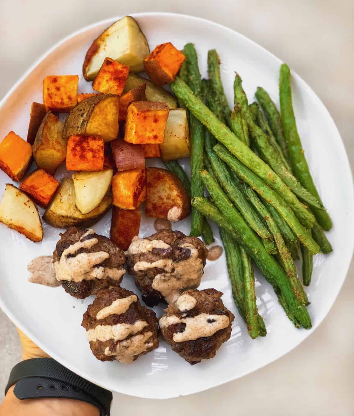Plate of meatballs covered in tahini sauce, green beans, and roasted potatoes