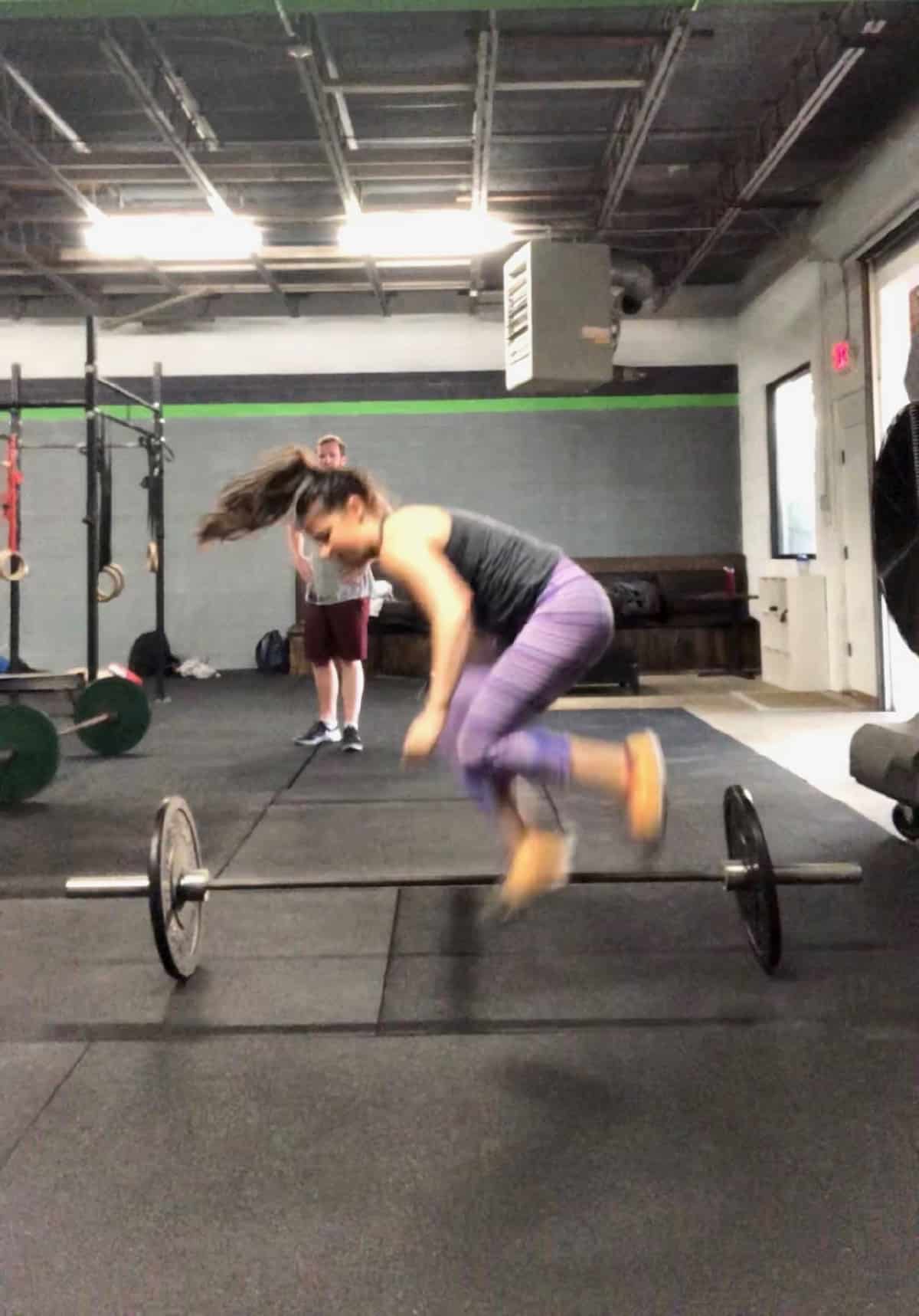 Girl jumping over a barbell doing lateral burpees