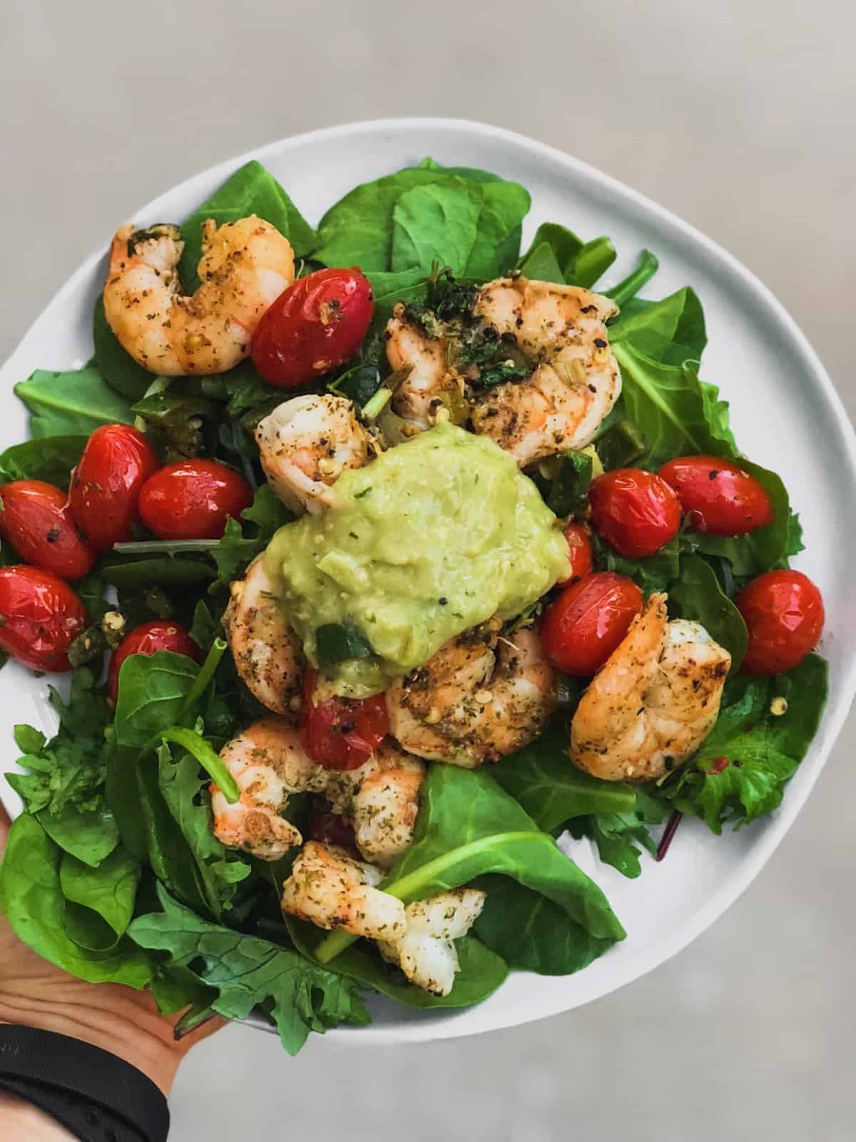 White plate with mixed greens, sautéed shrimp and tomatoes, and tomatillo salsa