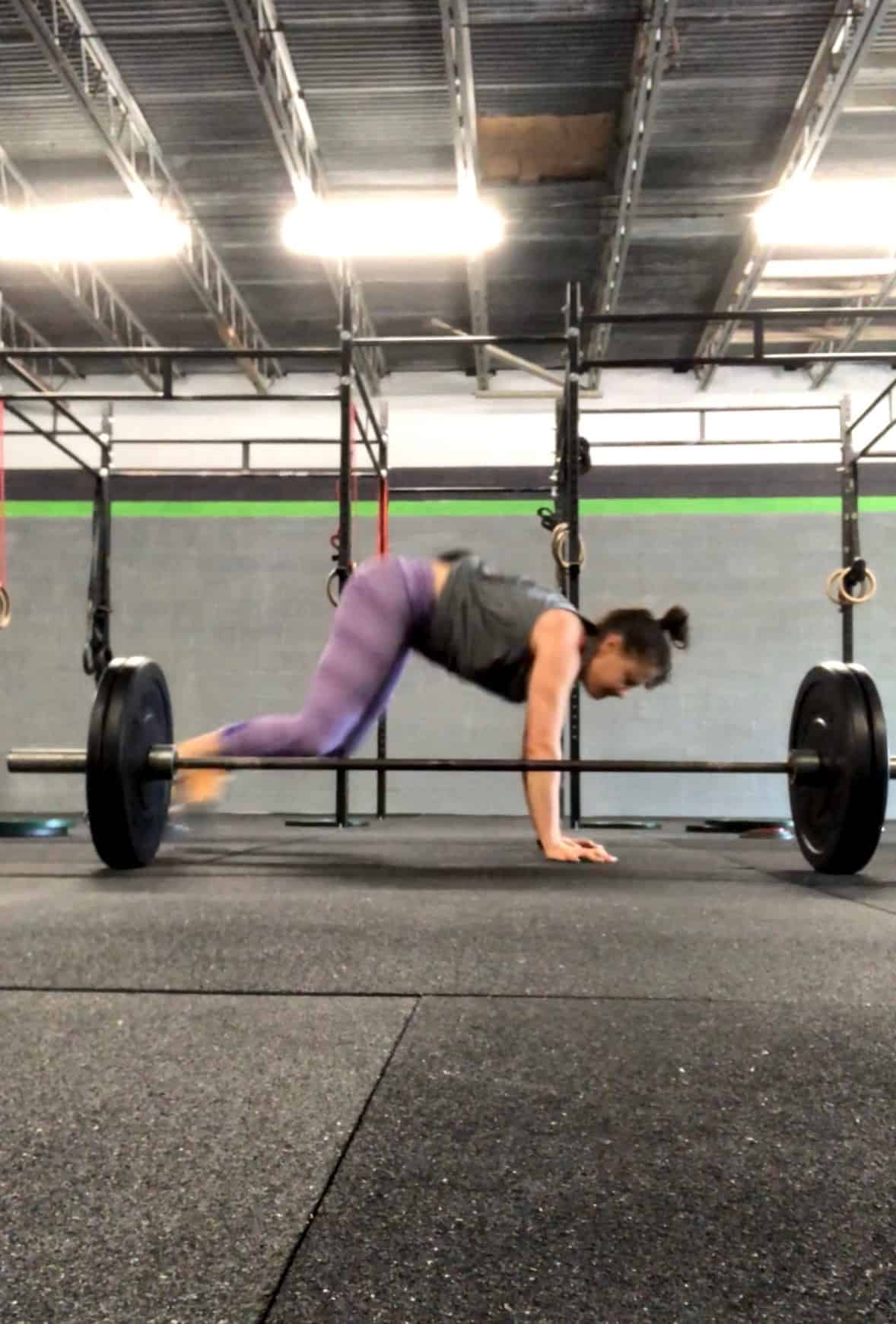 Girl doing a lateral burpee over a barbell