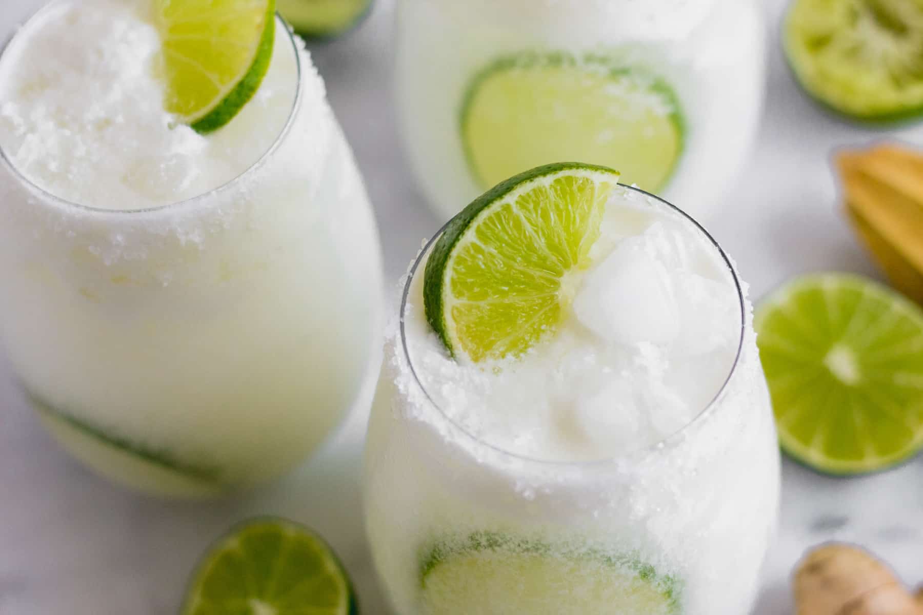 Three glasses filled with coconut lime mocktail on a white countertop surrounded by limes