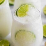 Glass with a salted rim filled with a coconut mocktail and limes