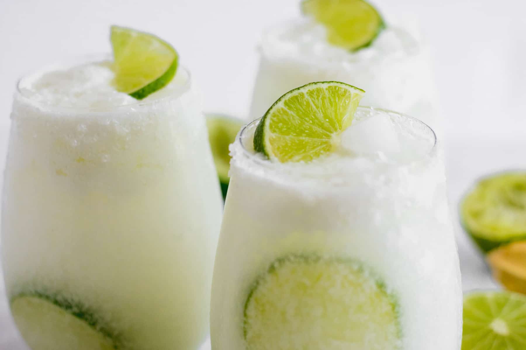 Three glasses filled with coconut lime mocktail garnished with lime wedges