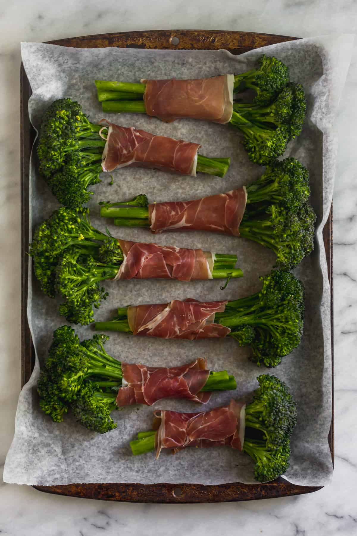 Pan of broccolini wrapped in prosciutto before it will be baked in the oven