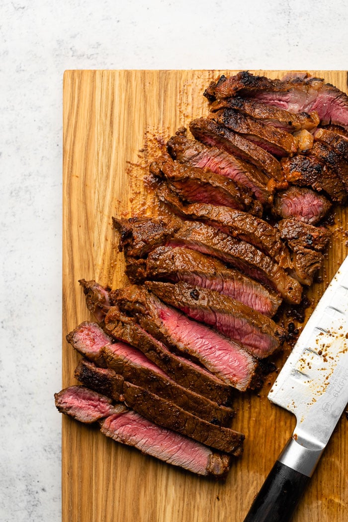 A cutting board with sliced steak on it and a knife.