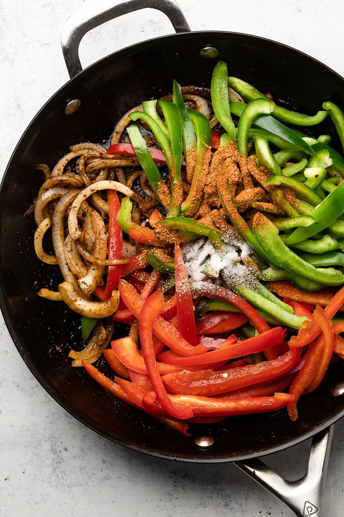 Large pan with cooked onion, raw julienned peppers, and seasonings.