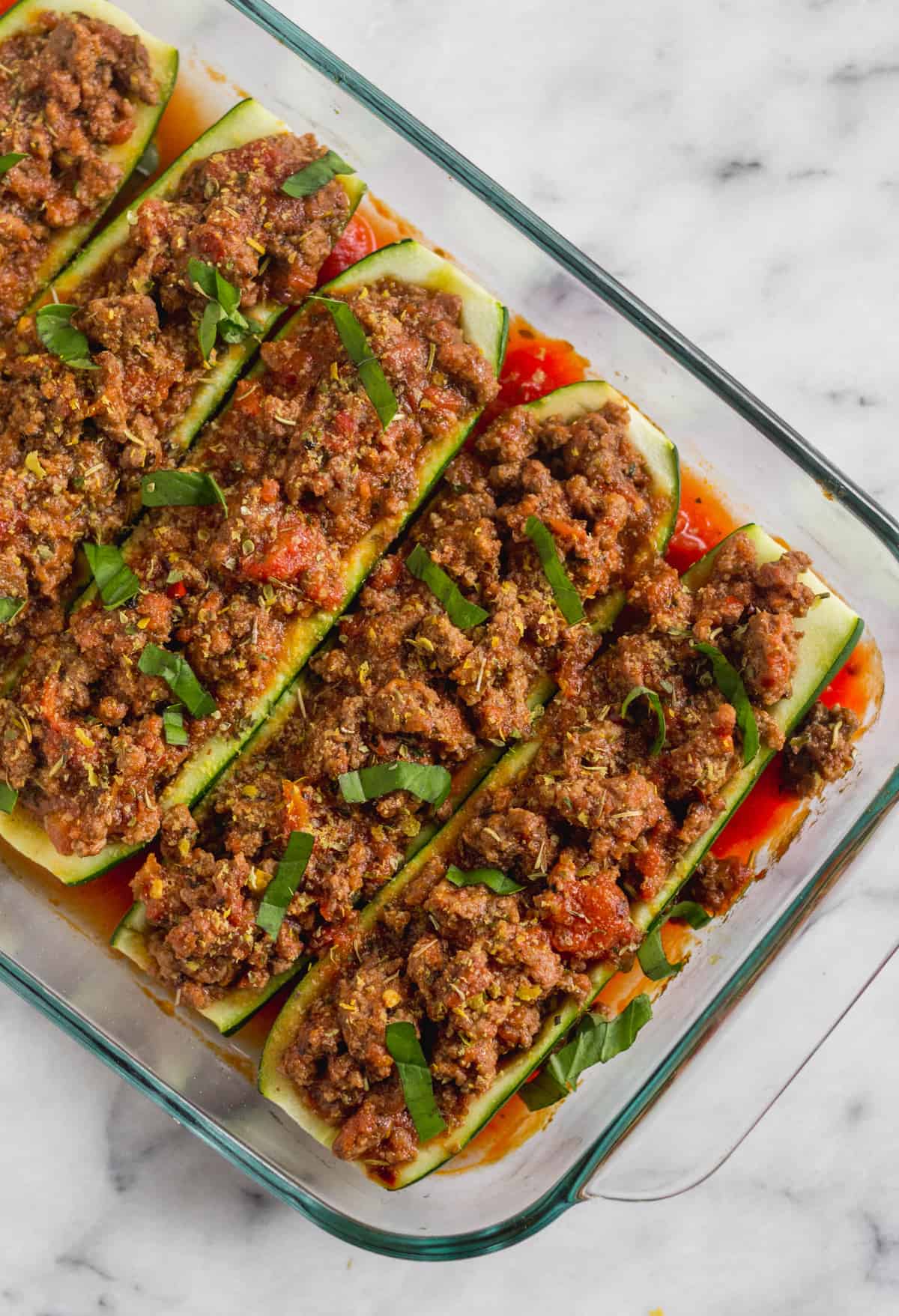 Pan filled with zucchini boats stuffed with Italian seasoned beef and tomato sauce topped with fresh basil