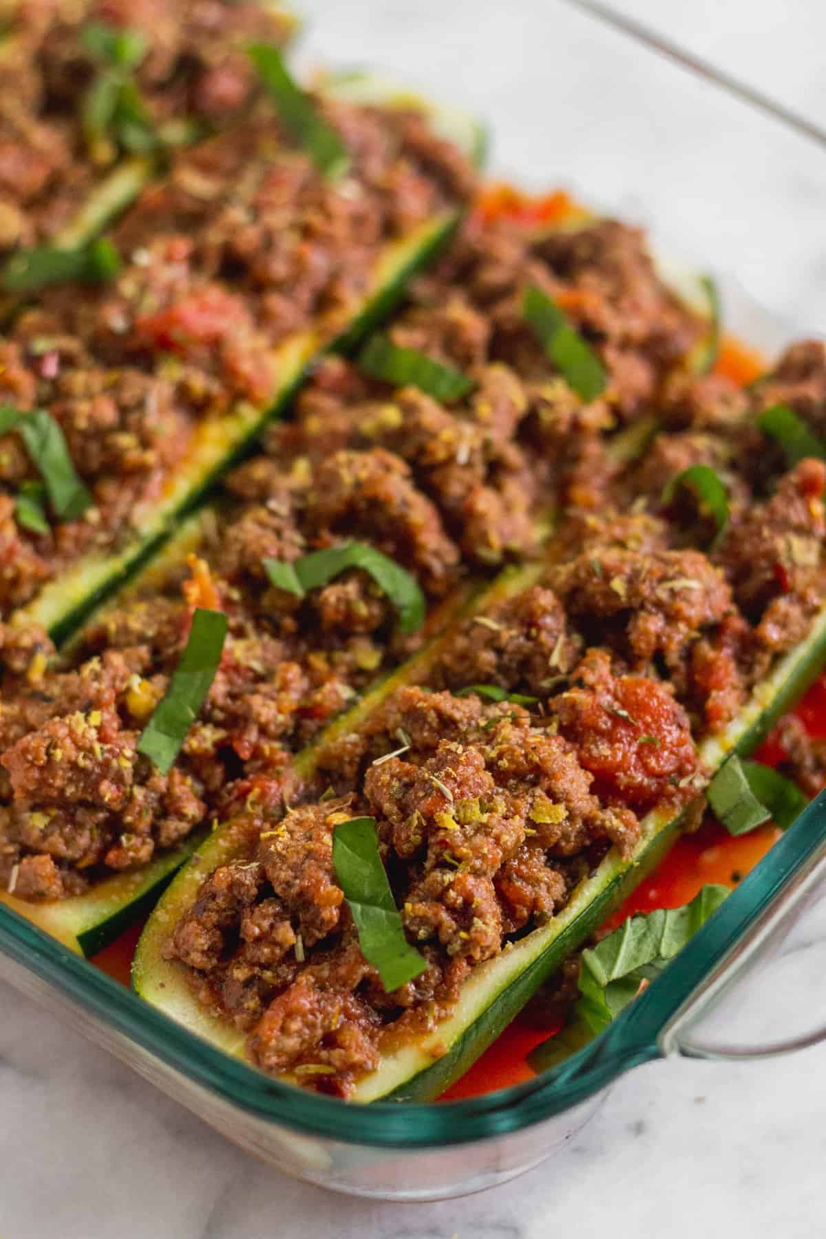 Glass baking dish filled with Italian beef stuffed zucchini boats topped with fresh basil
