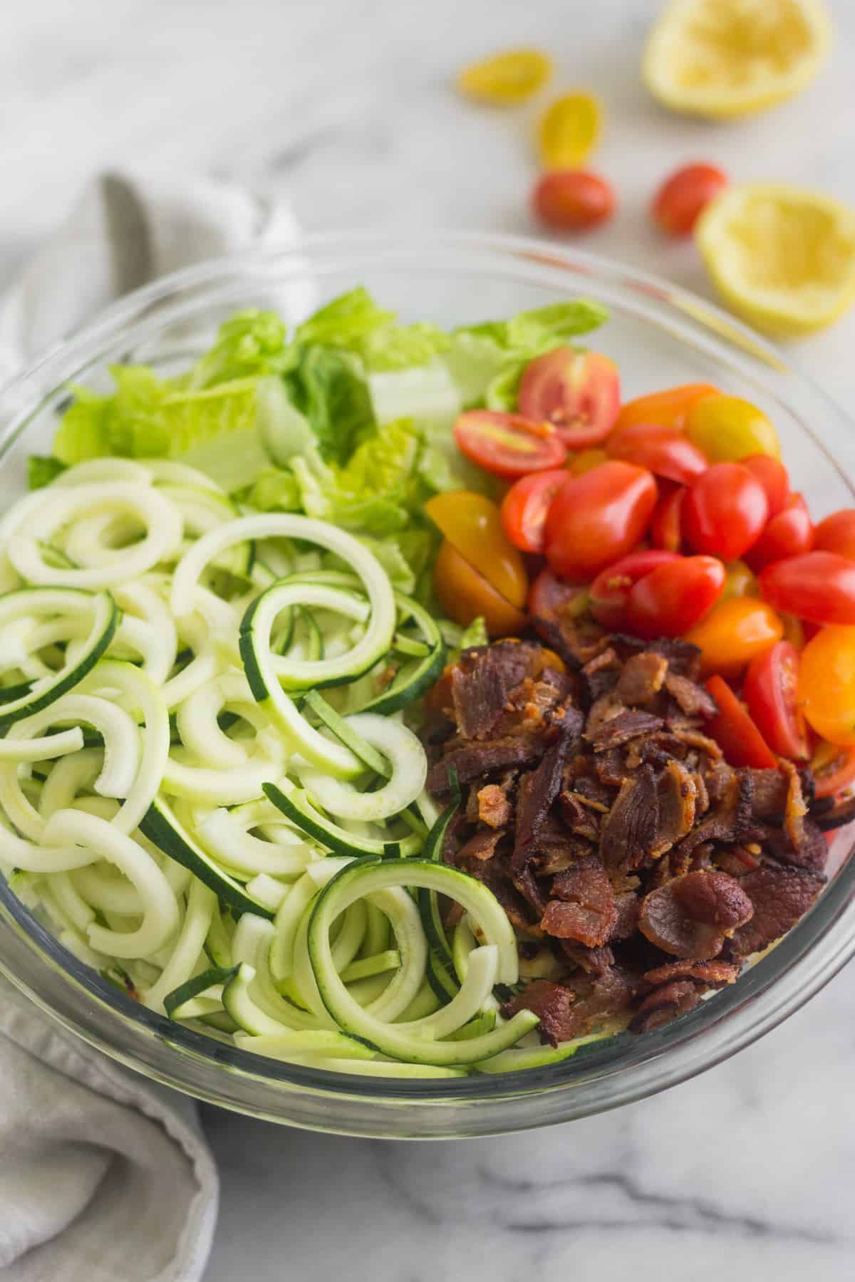Large glass bowl with zucchini noodles, chopped romaine, cherry tomatoes, and bacon for BLT Zucchini Noodle Pasta Salad