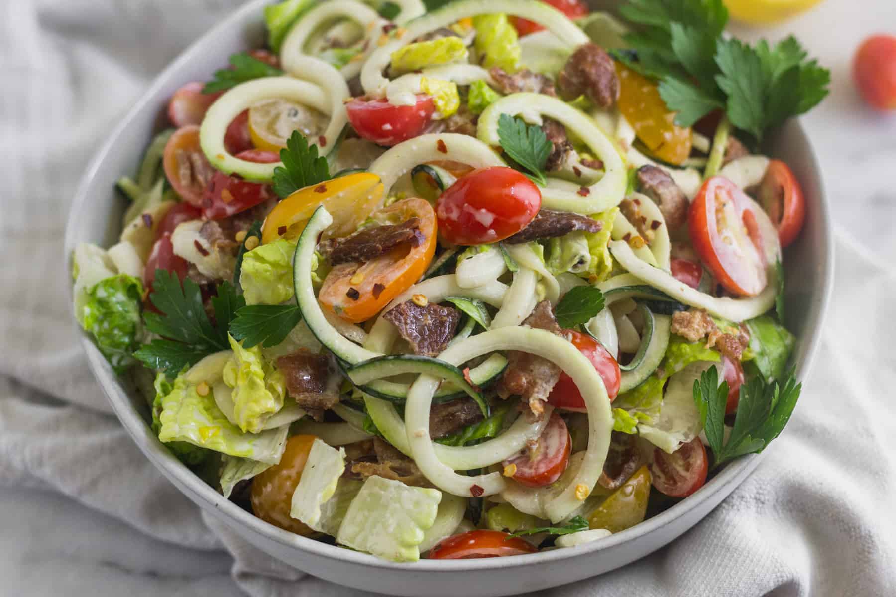 Close up of Large glass bowl with zucchini noodles, chopped romaine, cherry tomatoes, and bacon for BLT Zucchini Noodle Pasta Salad