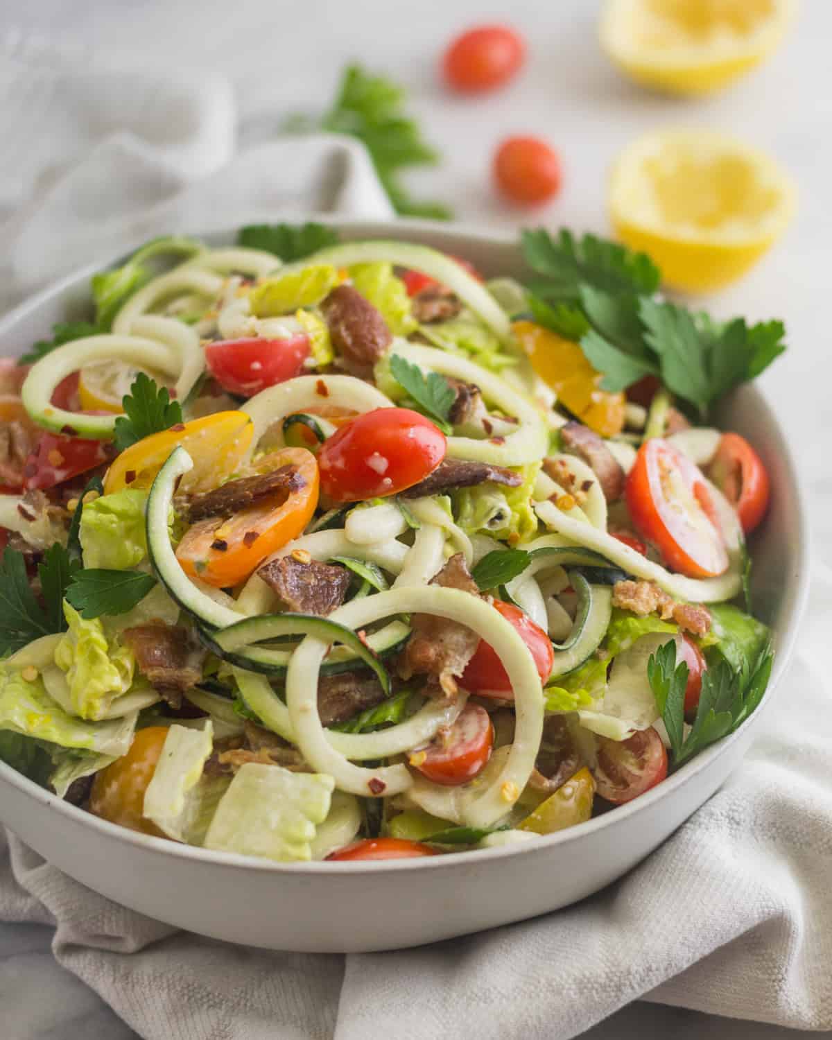 Large white bowl of BLT Zucchini Noodle Pasta Salad with half a lemon and cherry tomatoes behind it
