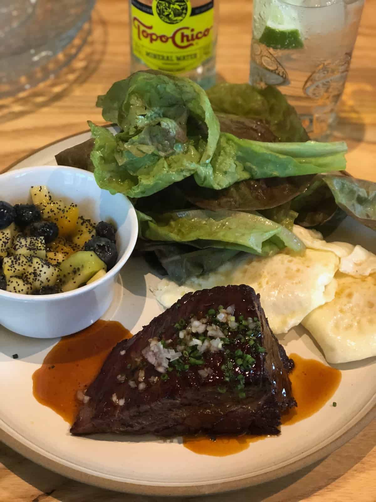 Steak and eggs with some greens and bowl of fruit