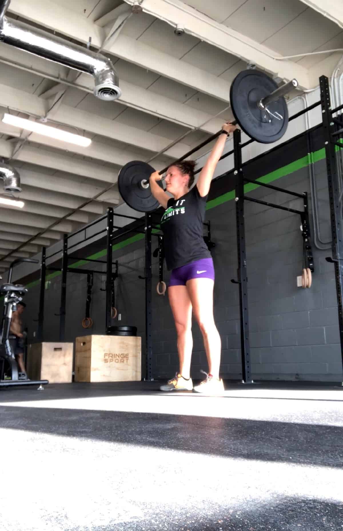 Girl holding a barbell over her head after doing a snatch