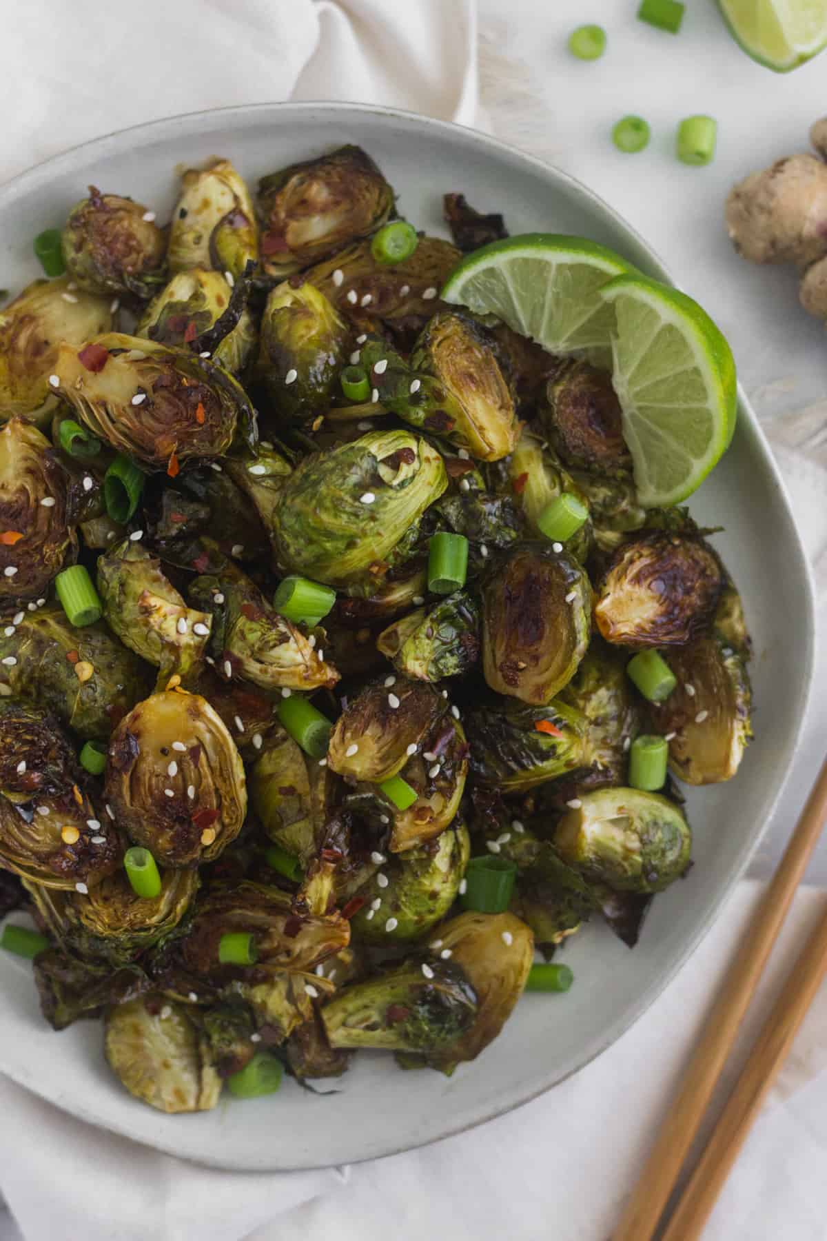 Plate of miso glazed brussels sprouts garnished with green onions, sesame seeds, and lime wedges