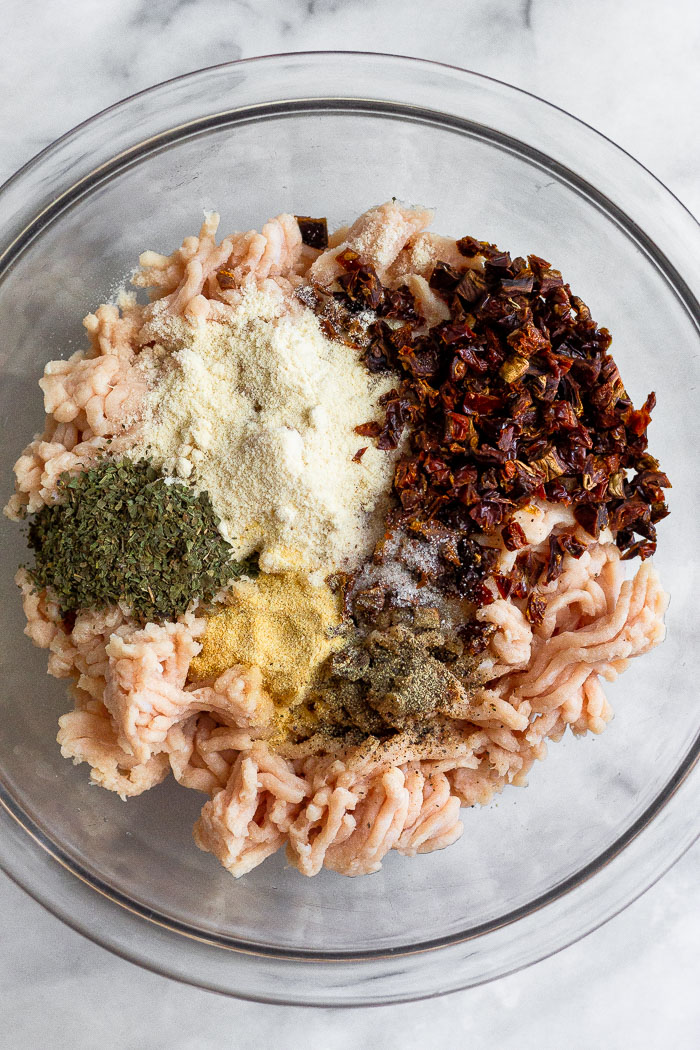 Bowl of ground chicken, sun-dried tomatoes, coconut flour, basil, and garlic.