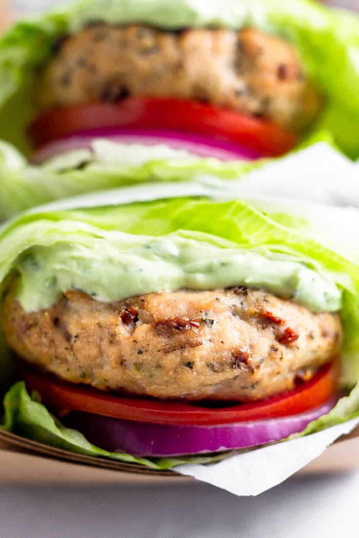 Basket of two grilled chicken burgers with tomato, onion, and basil aioli in lettuce wraps in a basket.