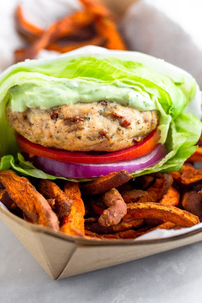 Sun-dried tomato chicken burger wrapped in lettuce sitting in a basket of sweet potato fries.