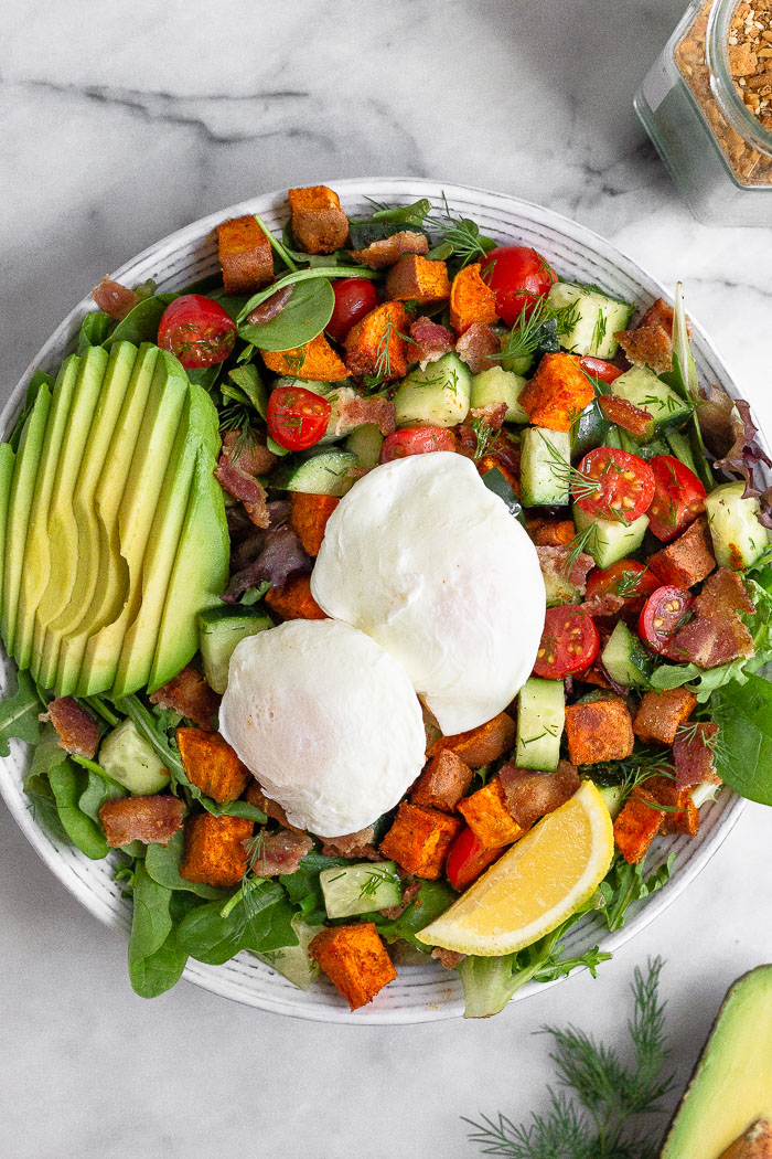 Avocado egg breakfast salad with two poached eggs on a large plate. Next to it is half an avocado and a jar of spice mix.
