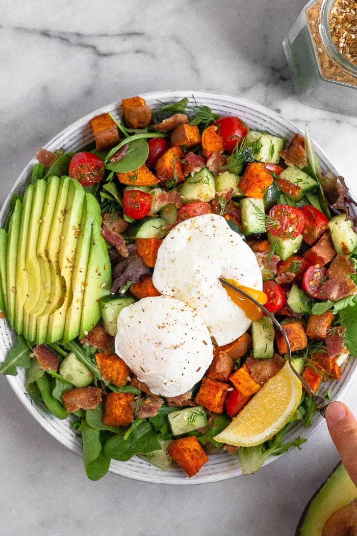 Overhead shot of a breakfast salad with poached eggs with a fork breaking open one of the eggs.