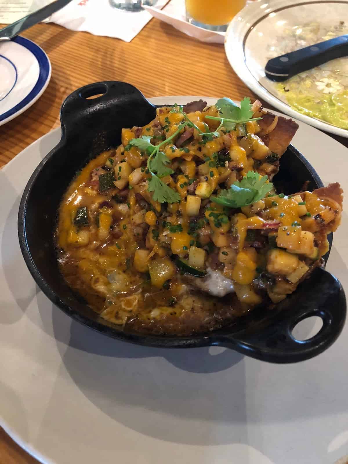 Small cast iron of summer nachos with chips, zucchini salsa, corn, and melted cheese