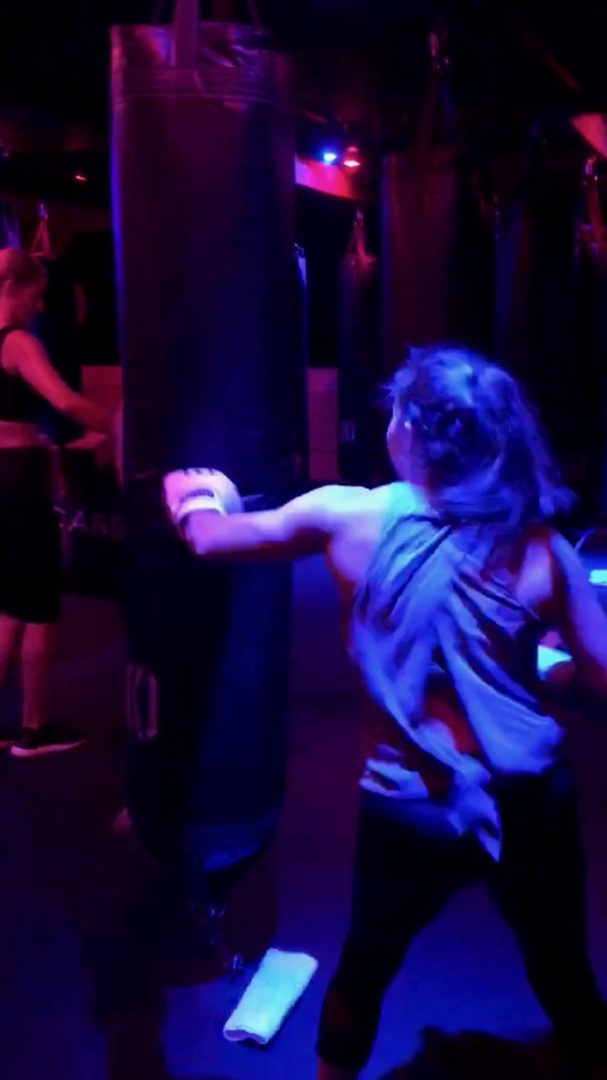 Girl doing a kickboxing class and punching a bag in a dar room