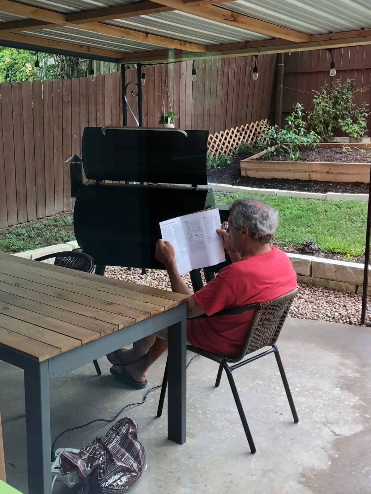 Man reading a manual for a Traeger grill with a Traeger grill behind him