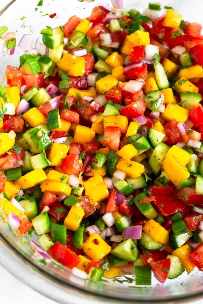 A close up of a bowl of mango tomato salsa with cucumber and red onion.