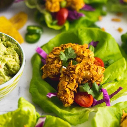 Lettuce wrap filled with a Paleo Plantain Crusted Crispy Shrimp Tacos next to a bowl of guacamole