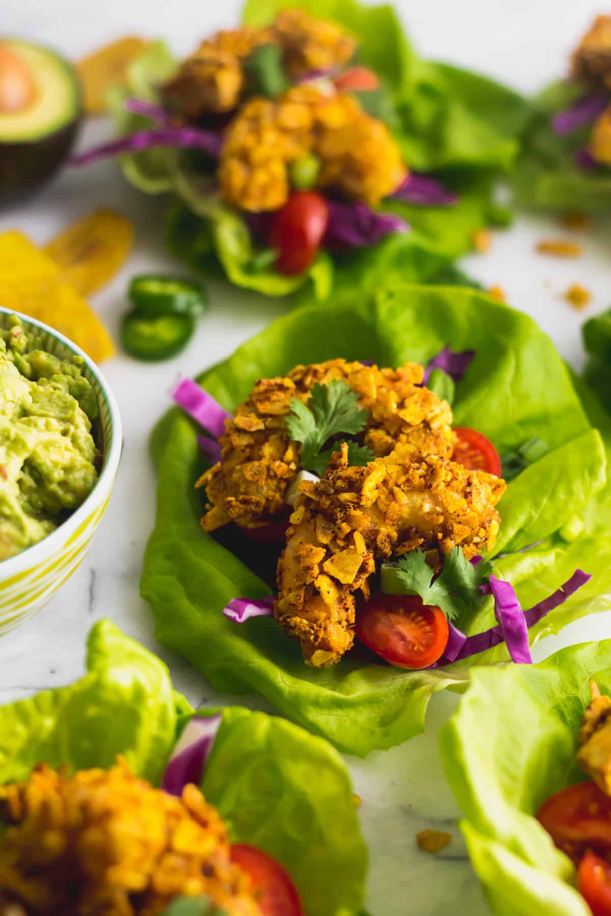 Lettuce wrap filled with a Paleo Plantain Crusted Crispy Shrimp Tacos next to a bowl of guacamole