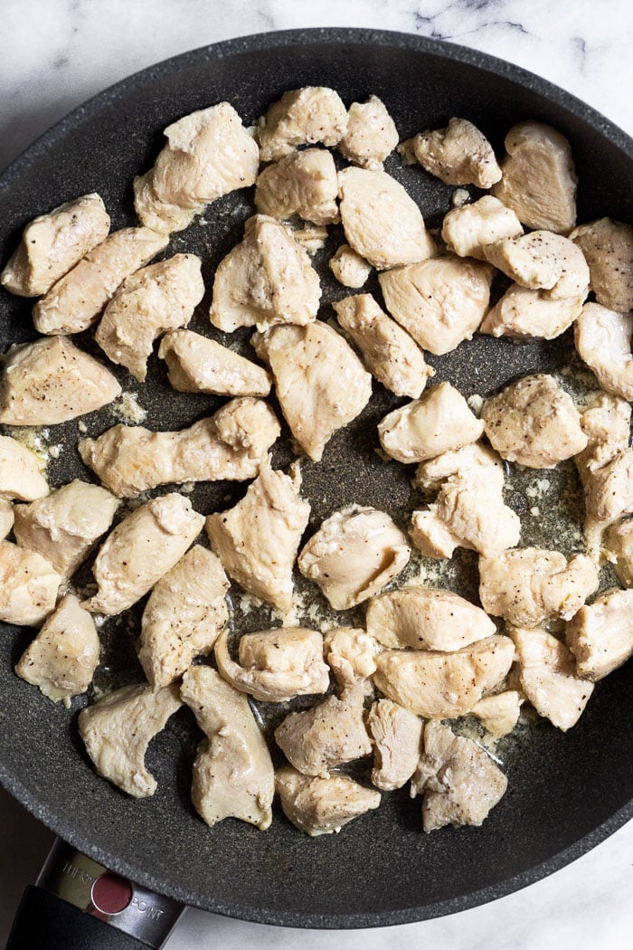 Saute pan with cooked pieces on chicken in it.