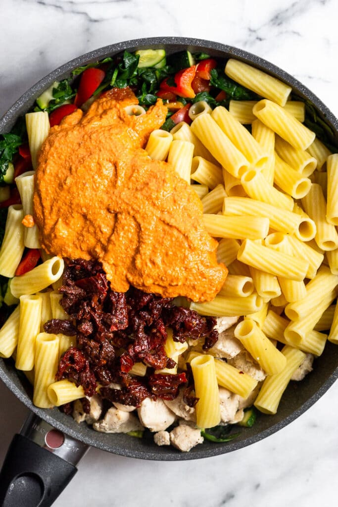 Pan filled with sautéed chicken, cooked pasta, veggies, and sun dried tomato sauce before it is all mixed together.