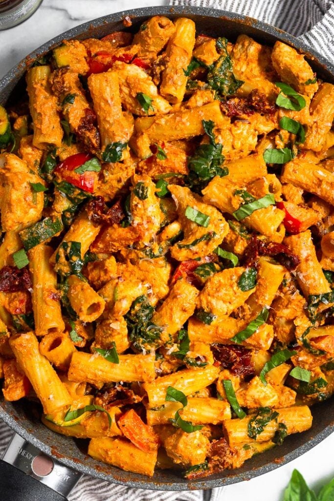 Overhead shot of a pan of creamy sun dried tomato pasta with chicken topped with fresh basil.