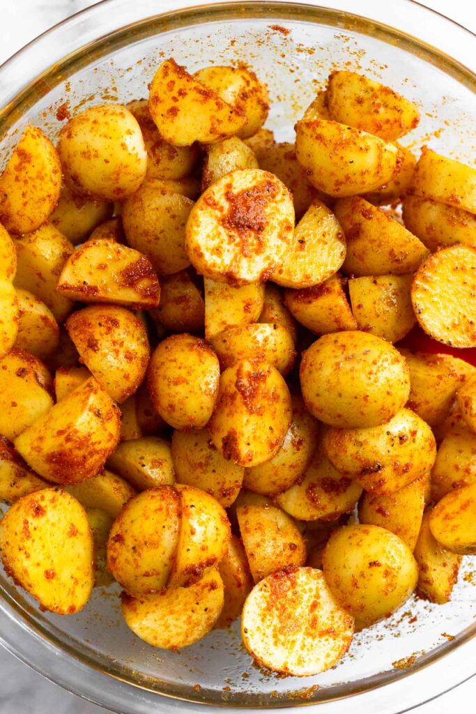 A bowl with diced white potatoes tossed with oil and spices.