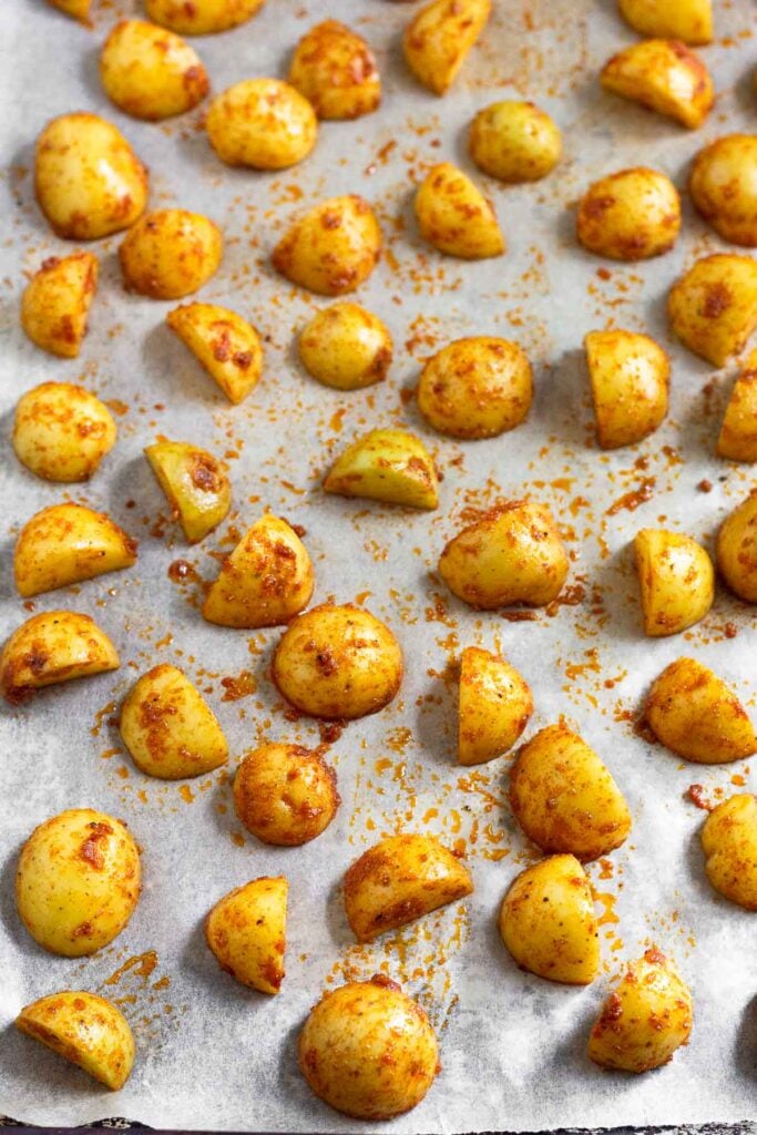 Baking sheet lined with parchment paper with diced potatoes coated in spices spread out on it.