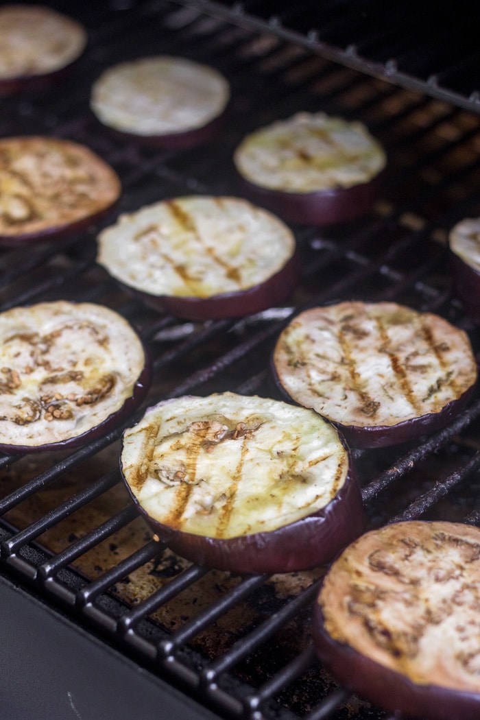 Grilled eggplant slices on the grates of a grill.