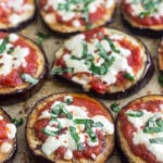 A bunch of eggplant pizza on baking sheet topped with basil and red pepper flakes.