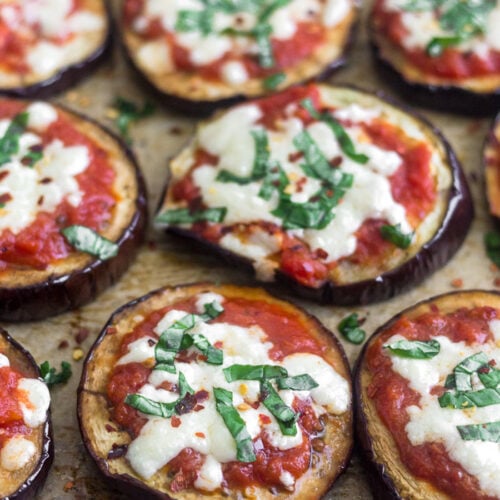 A bunch of eggplant pizza on baking sheet topped with basil and red pepper flakes.