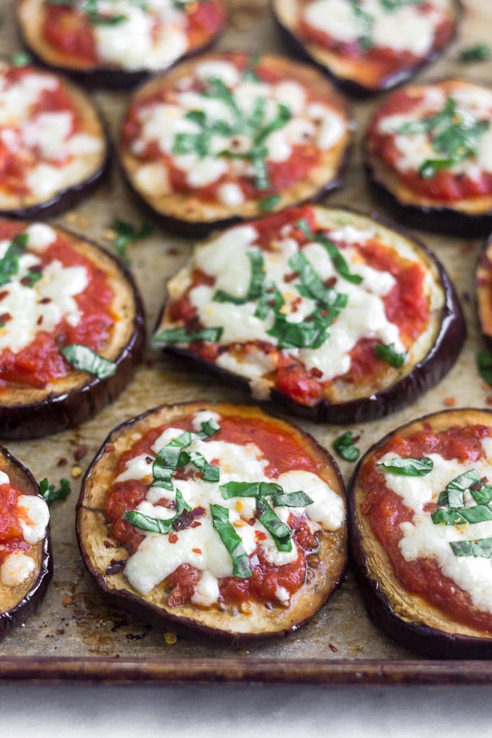 A bunch of eggplant pizza on baking sheet topped with basil and red pepper flakes.
