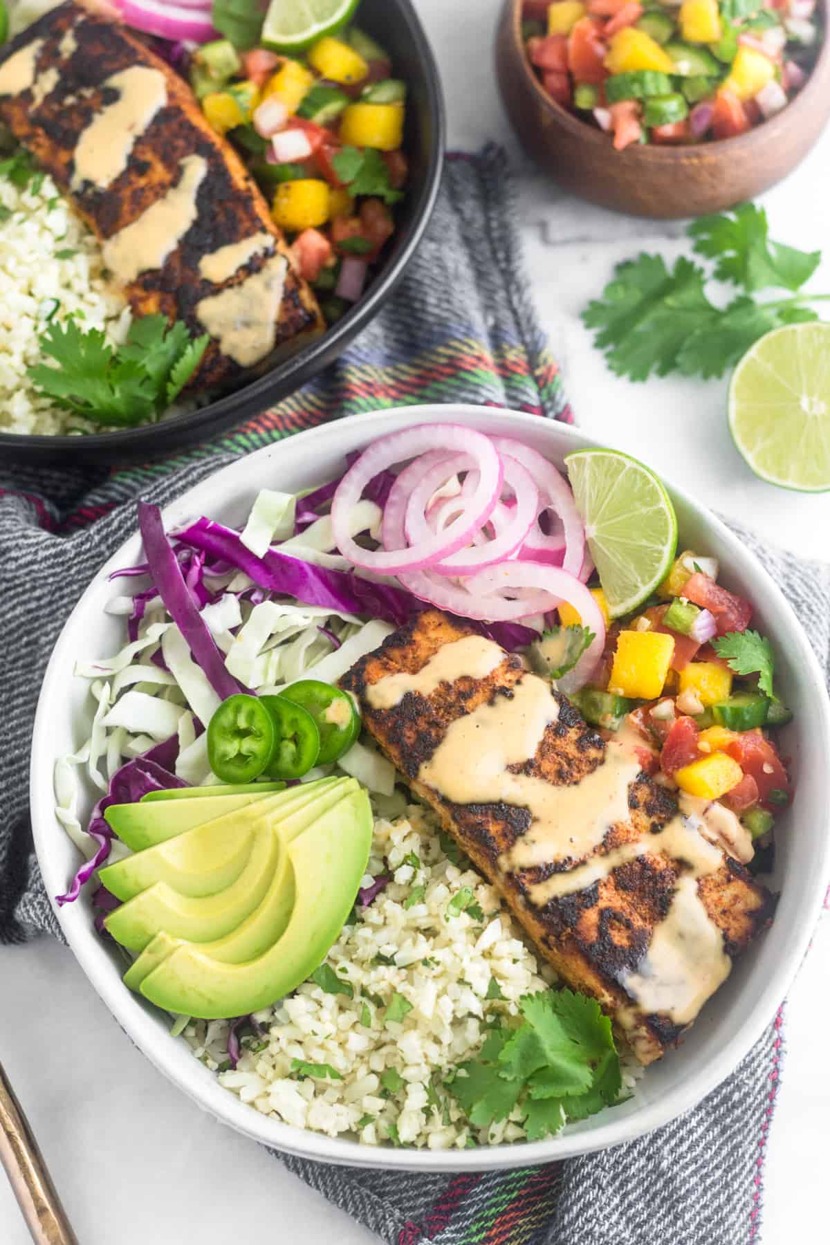 Two Whole30 fish taco bowl with blackened fish and chipotle mayo on top of a blue napkin on a white counter