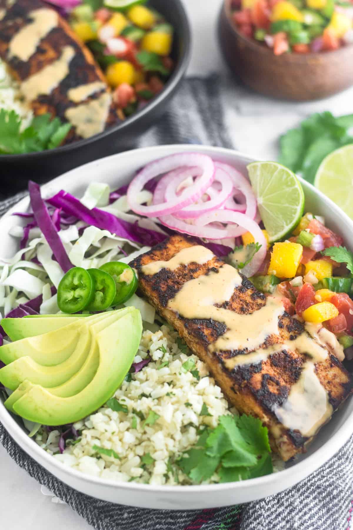 Whole30 fish taco bowl on top of a napkin with another fish taco bowl behind it and a bowl of mango salsa