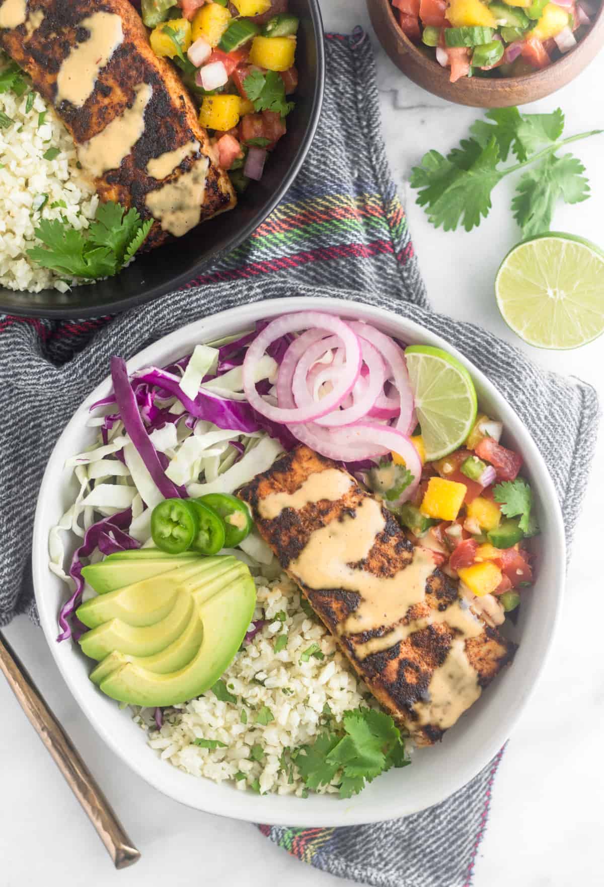 White bowl filled with a Whole30 fish taco bowl with cauliflower rice, shredded cabbage, pickled onions, mango salsa, avocado, blackened fish, and chipotle mayo