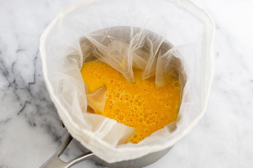 Small sauce pan with a nut milk bag in it and fresh fruit juice.