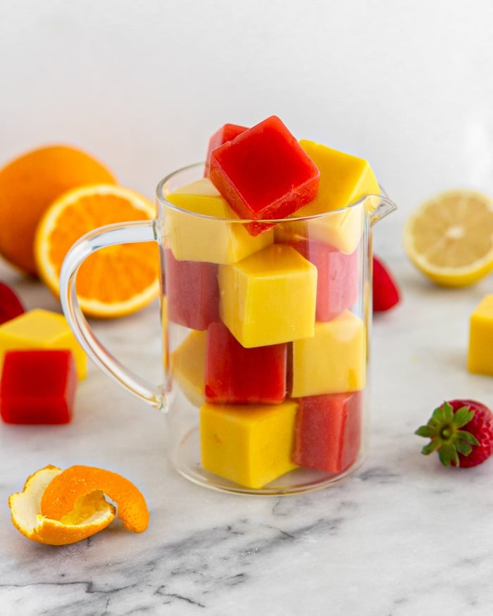 Glass jar filled with orange and strawberry homemade gummies. Around the jar is fresh fruit and more gummies.