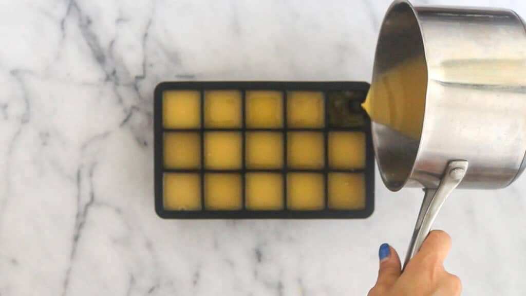 Overhead shot of a silicone ice cube tray with a pan pouring in homemade gummies that have not been set yet.