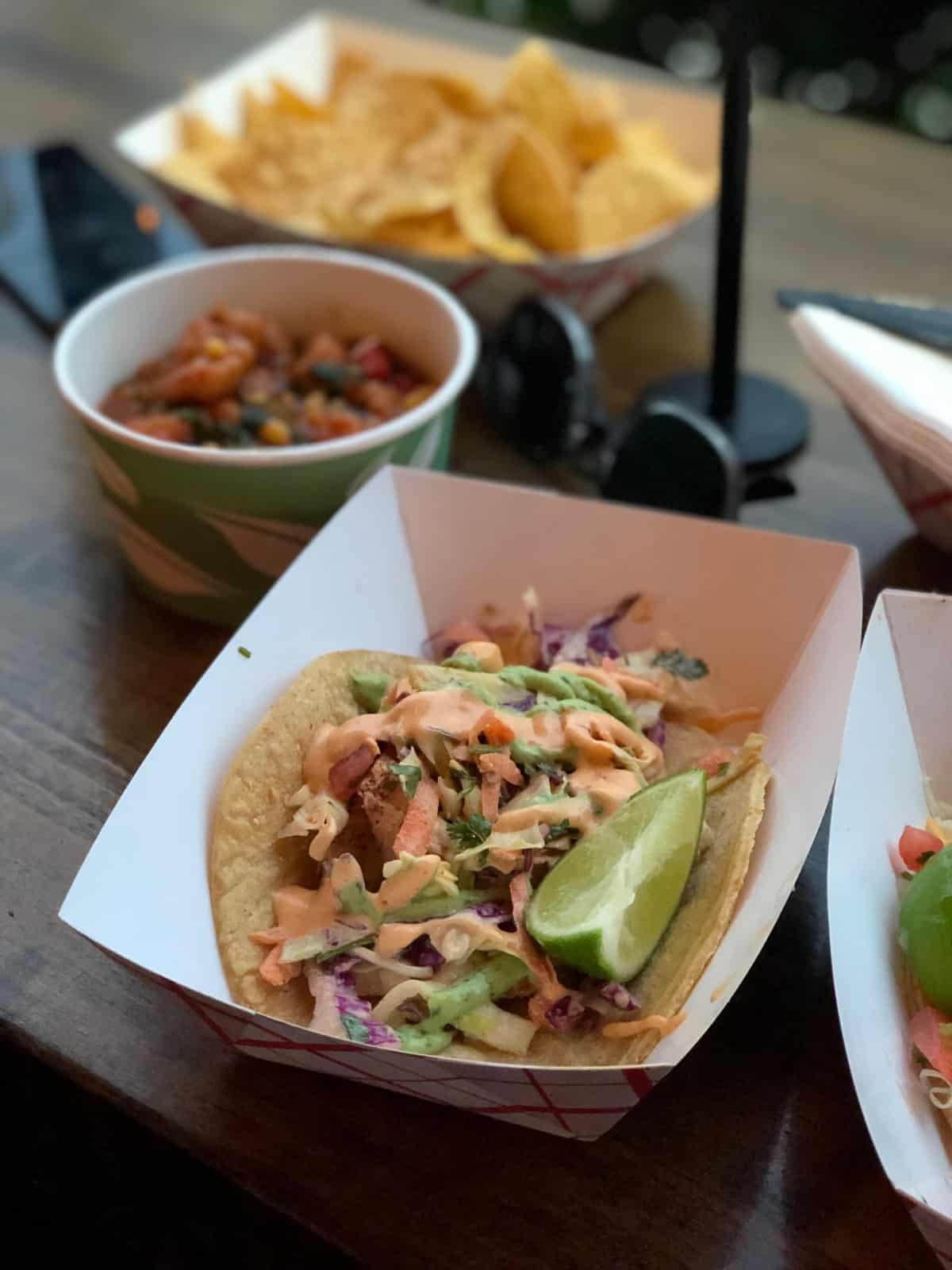 Fish taco with a lime wedge and ceviche and chips behind it