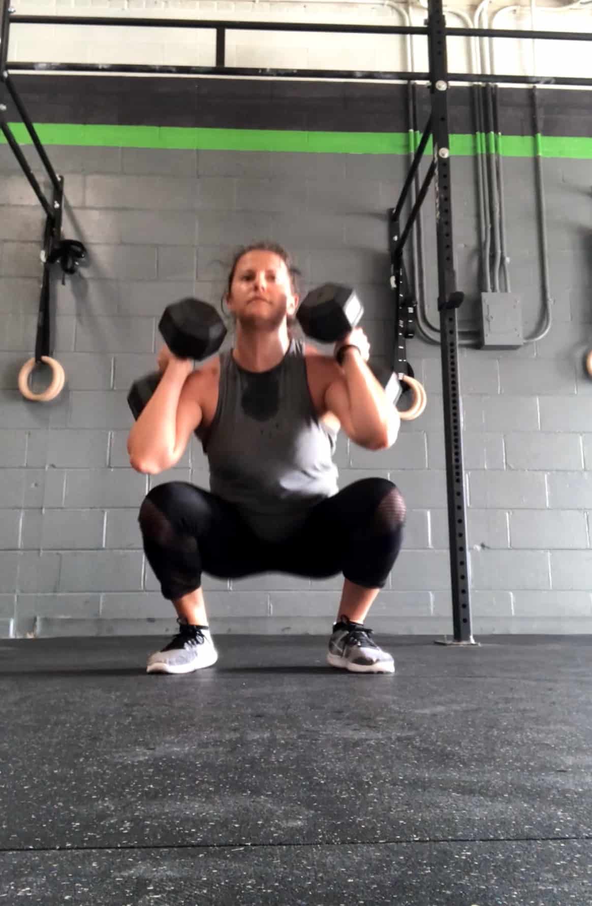 Girl in the bottom of a squat holding dumbbells on her shoulders doing dumbbell squat cleans