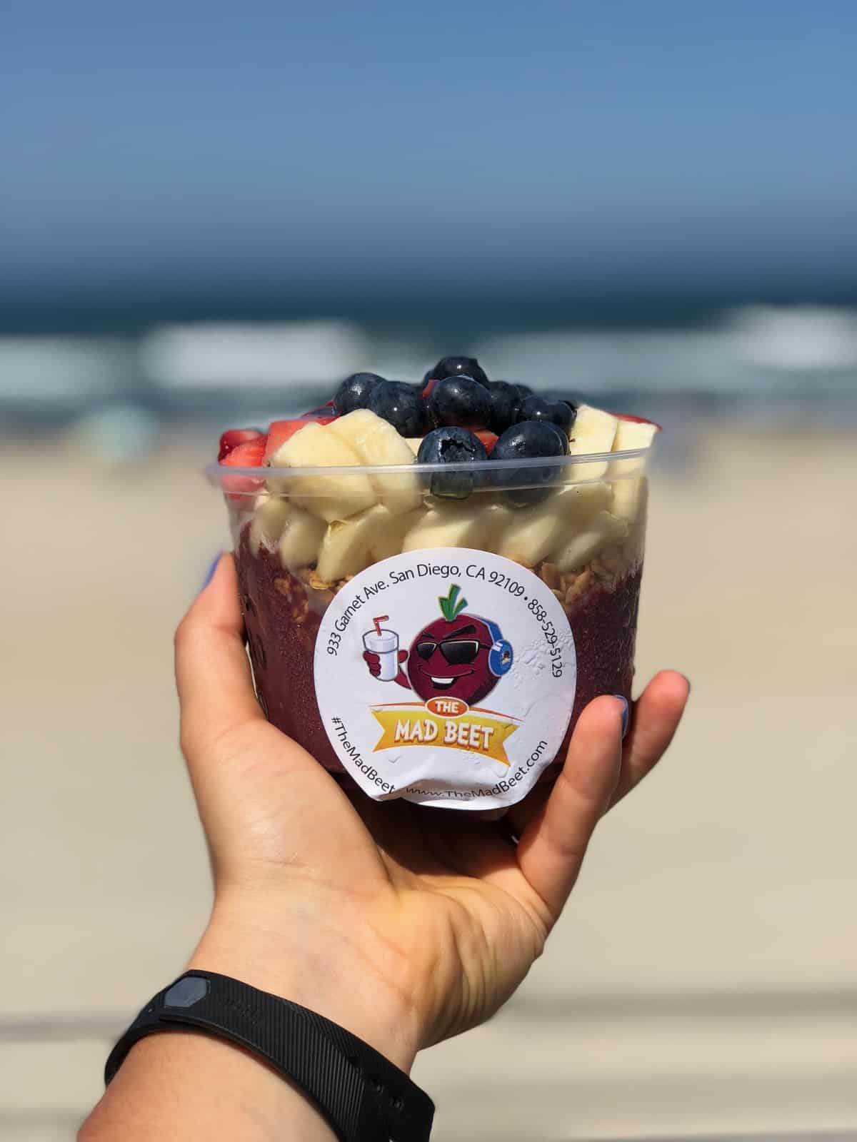 Acai bowl in a plastic container with the beach in the background